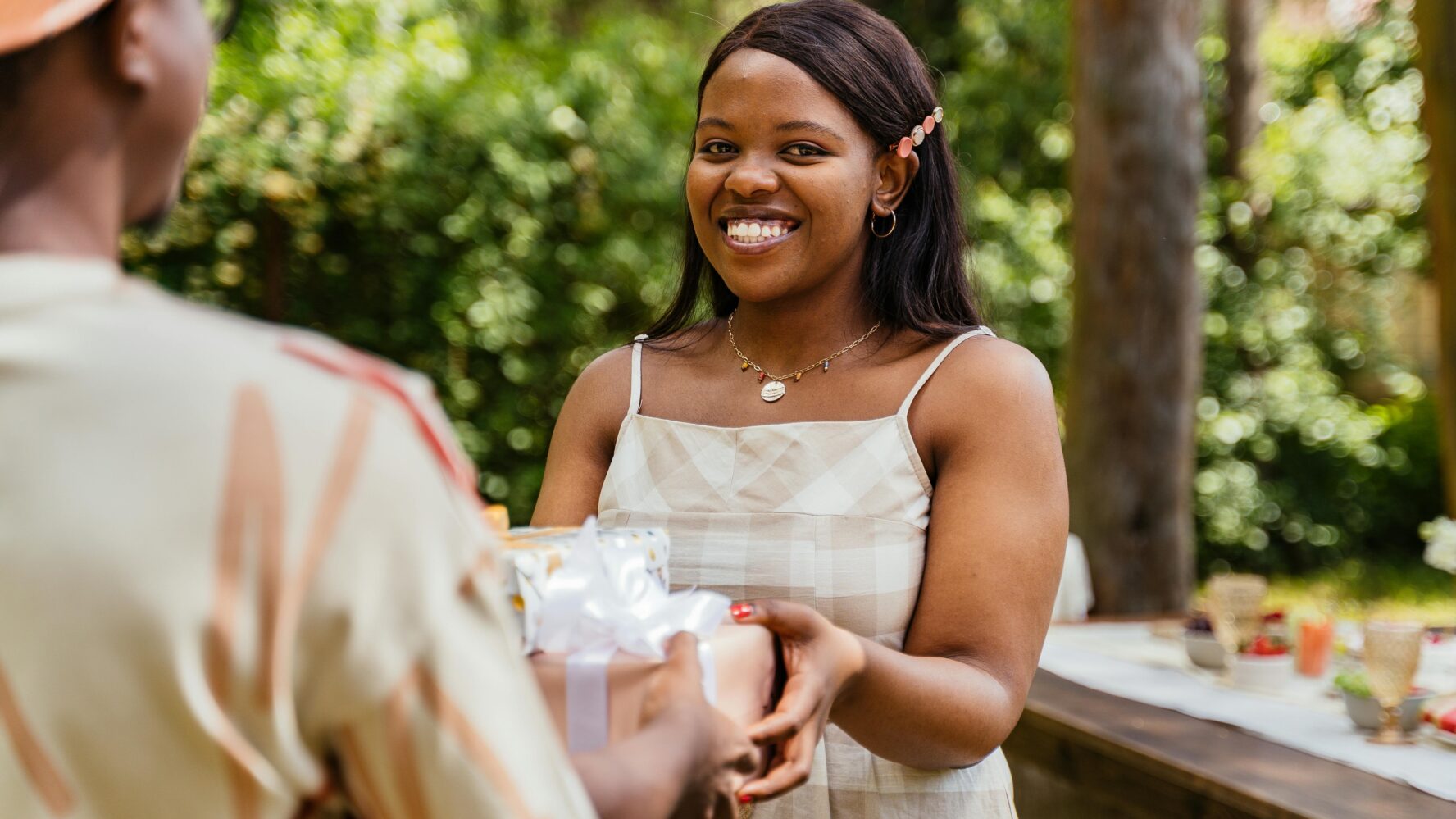 A young woman stood outside smiling at the camera while receiving a wrapped present
