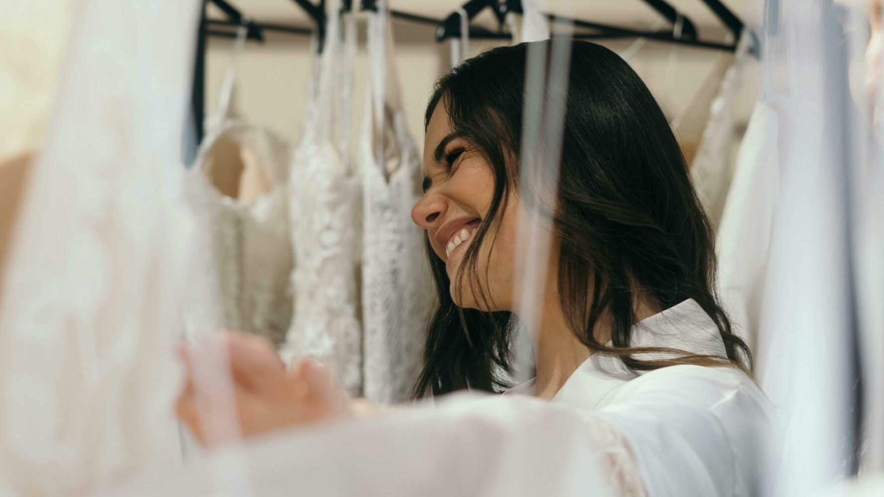 A bride peeping through rails of bridal gowns looking really happy. Photo by Los Muertos Crew / Cristian Rojas.