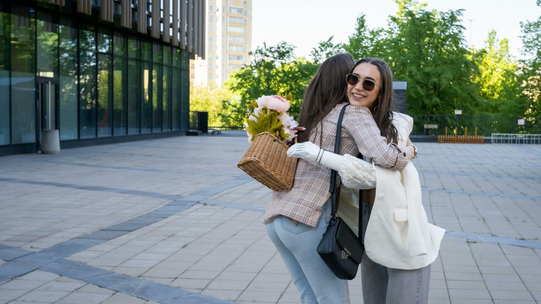 Image of two friends in their 20's hugging, one friend has a bionic arm and is giving her friend some flowers