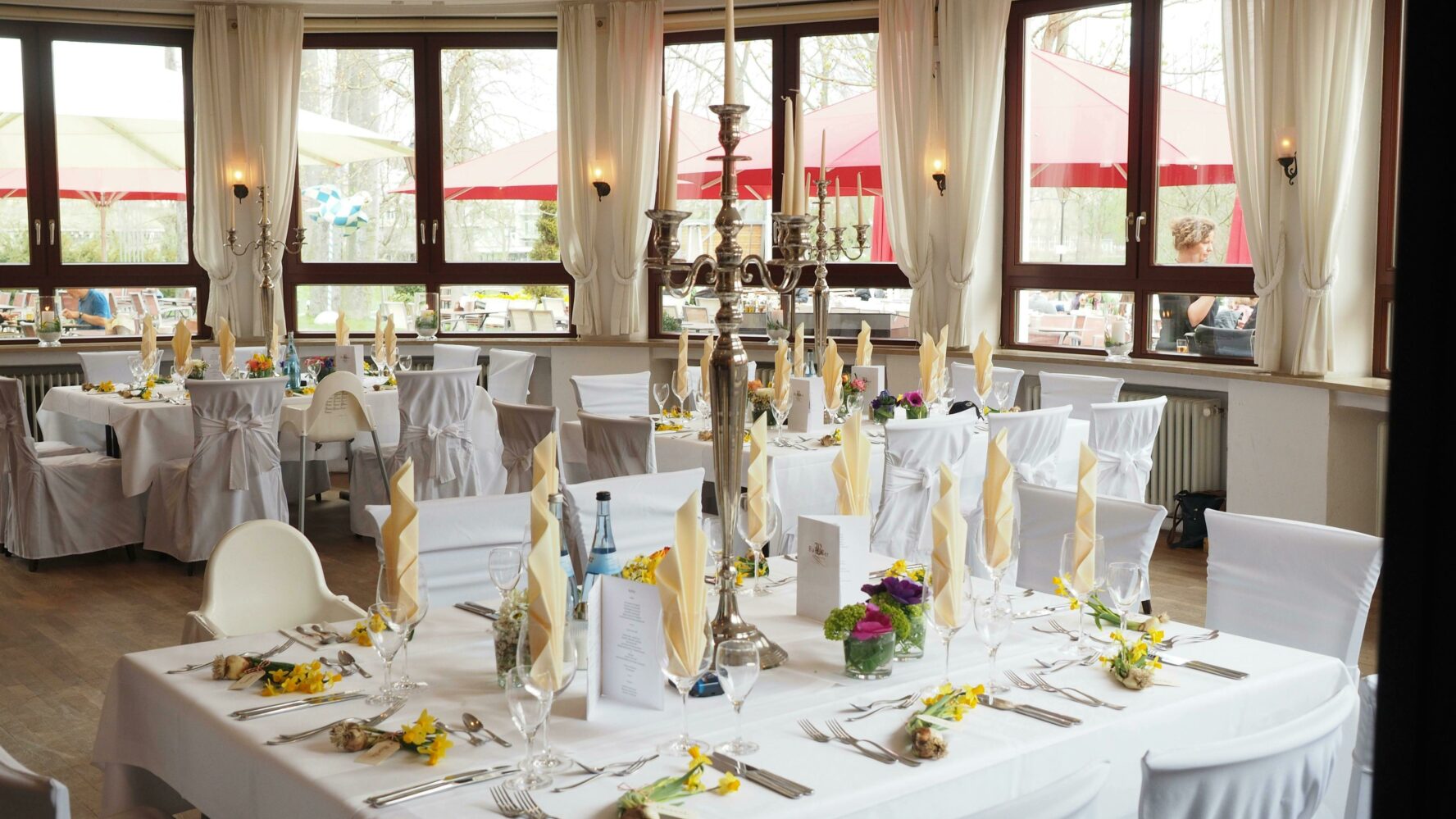 A pub function room decorated for a wedding, with white table cloths and chair cushions, silver candelabras in the centre of each table, cream napkins and little flowers at each seat.Photo by Pixabay.