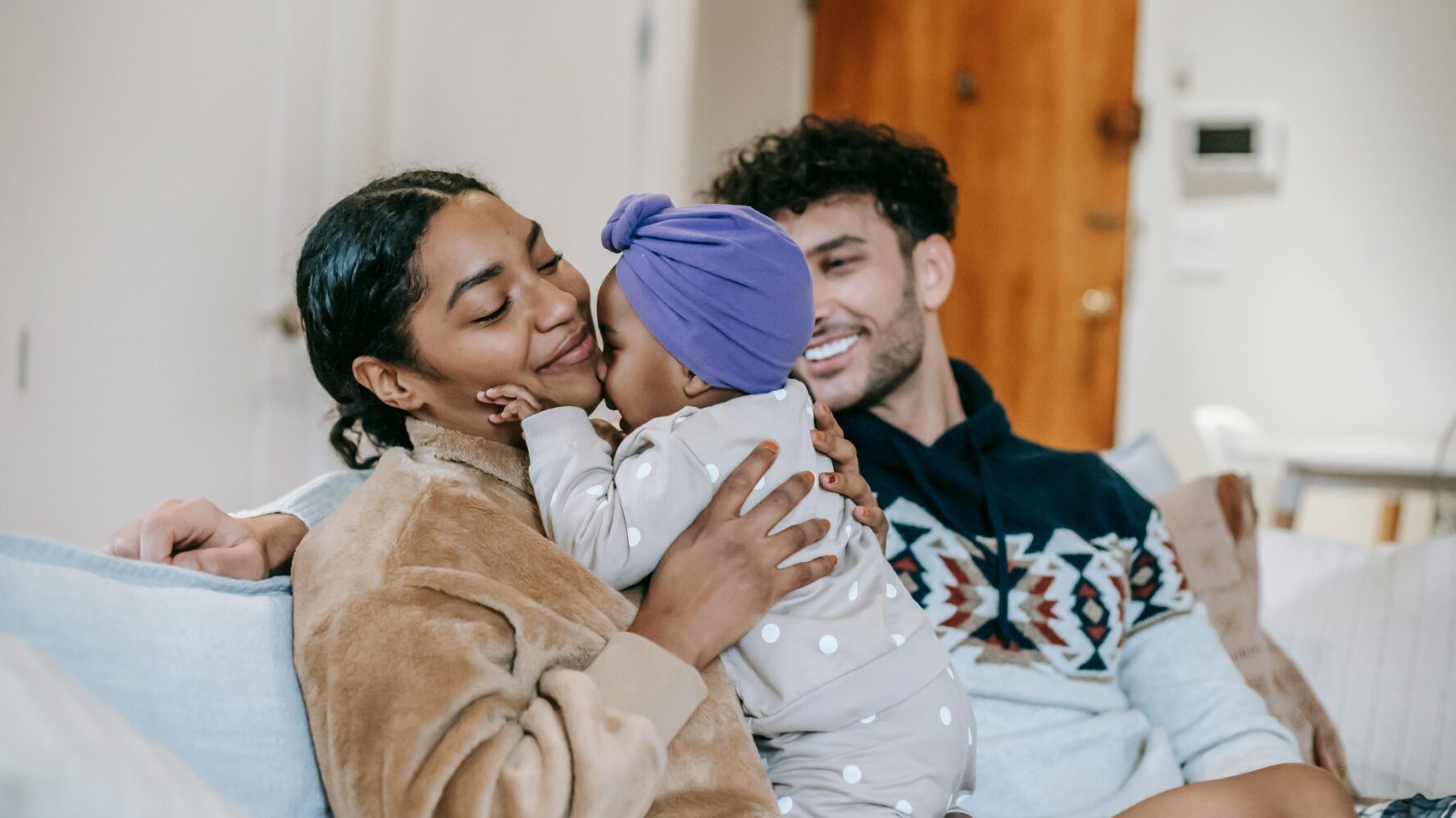 A mum and dad sat on their sofa, smiling at their baby