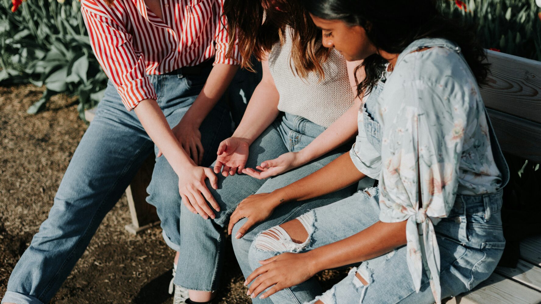 Three women sat on a bench with their hands rested on the woman in the middle, praying for her