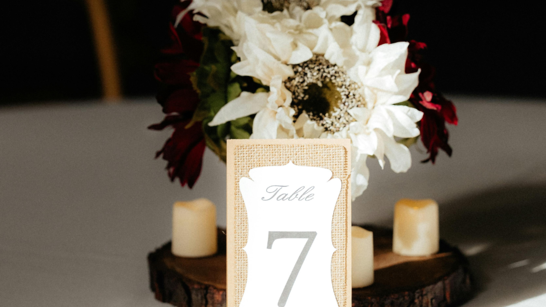 A hand-crafted card that sits on a table. Next to a bunch of flowers and couple of candles, it reads 'table 7'. Photo by Taylor Thompson (cropped from original)