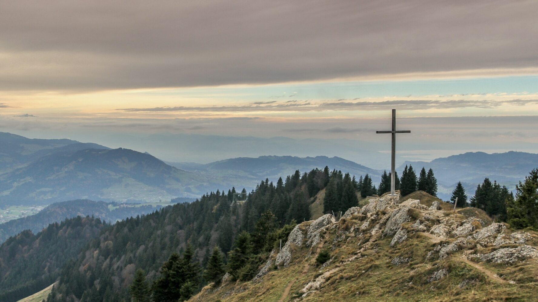 Image of a green hill landscape with a wooden cross on the top of the hill