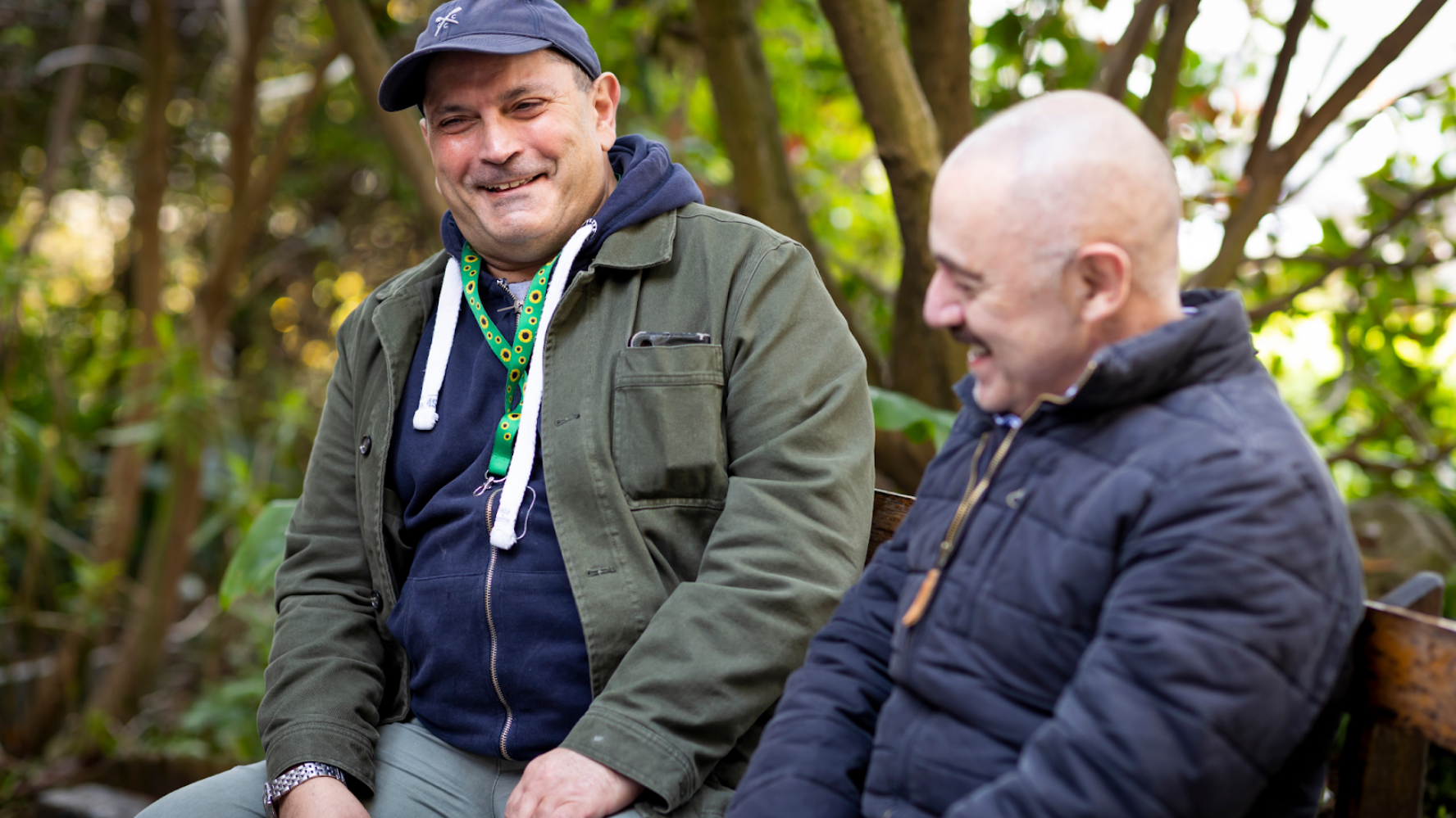 Two men sat on a bench smiling, one is wearing a sunflower lanyard
