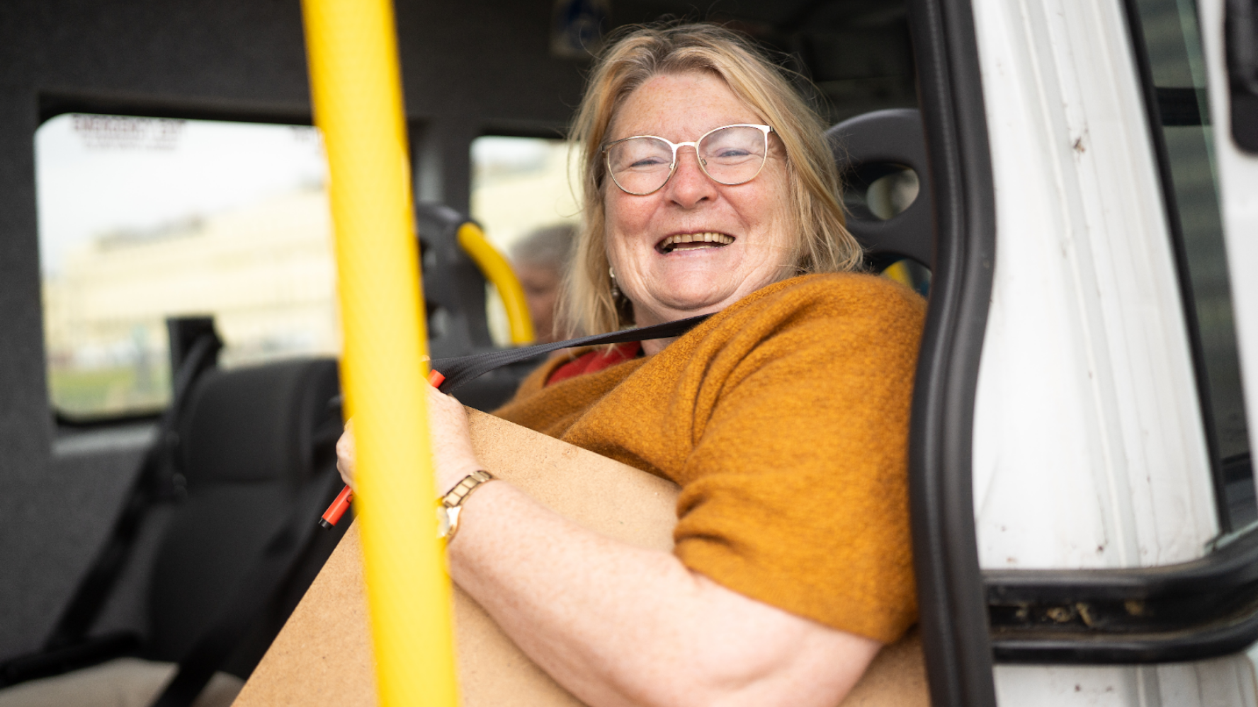 A lady sat on a minibus, smiling at the camera