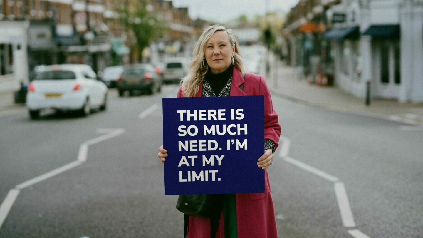 Ruth holding a sign that reads 'There is so much need. I'm at my limit.'