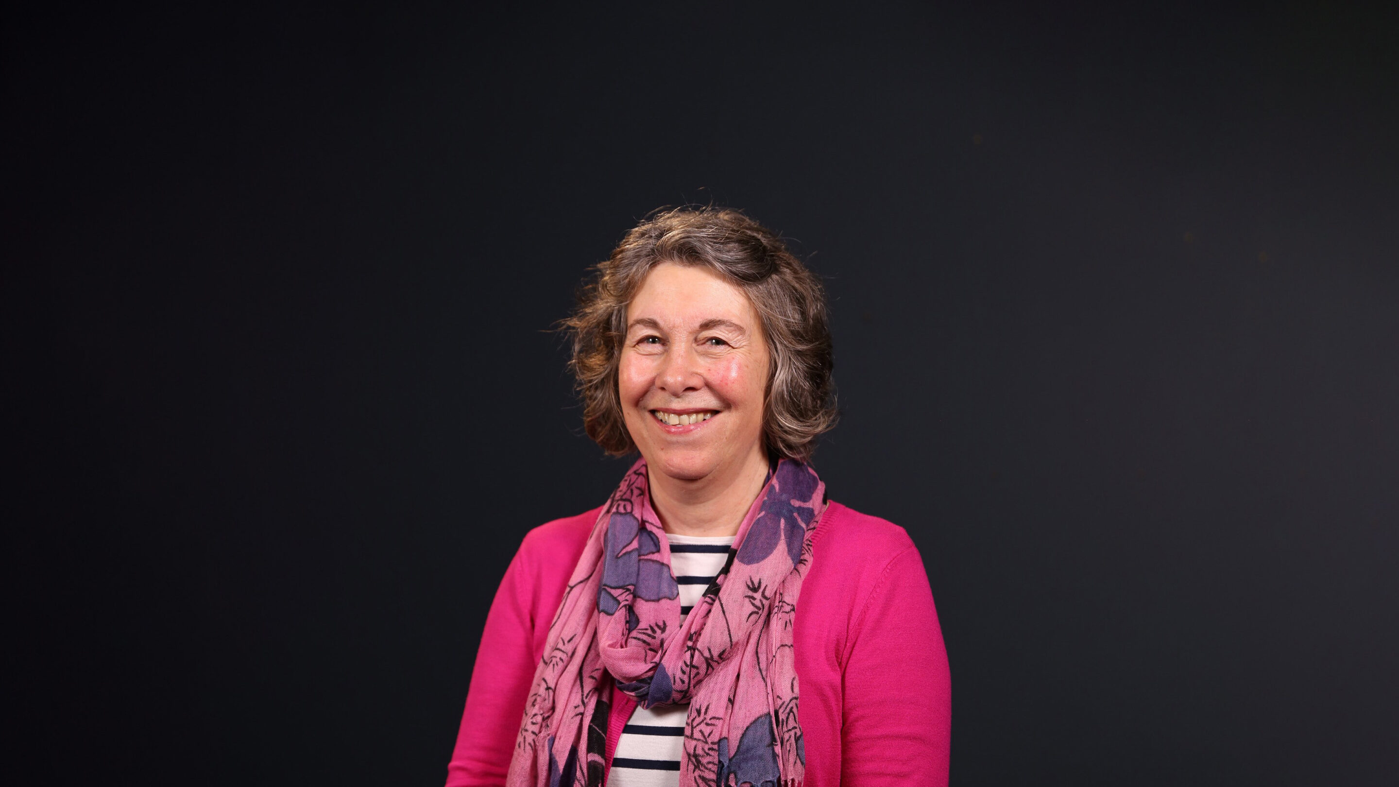 Older woman sat facing the camera smiling.