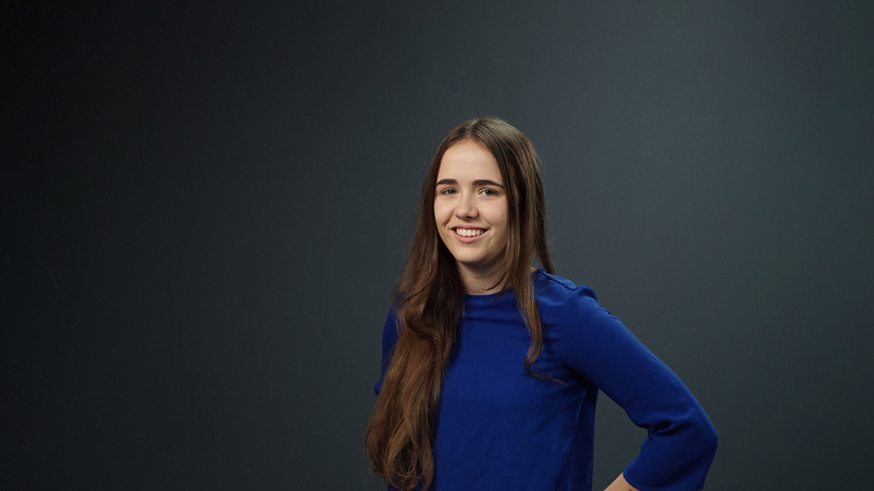 Young woman in a blue jumper stood smiling at the camera.