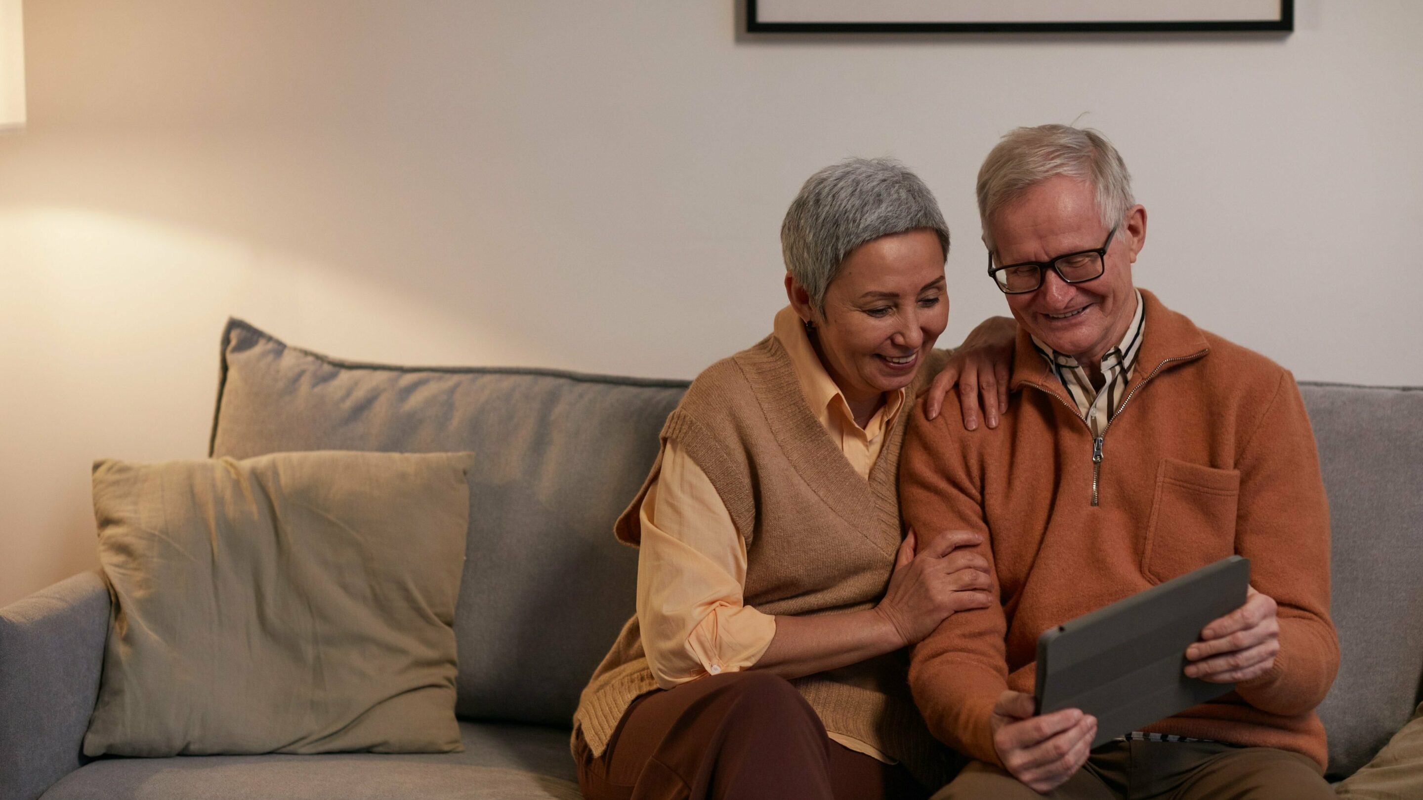A happy older couple sat on a sofa together looking at an iPad.