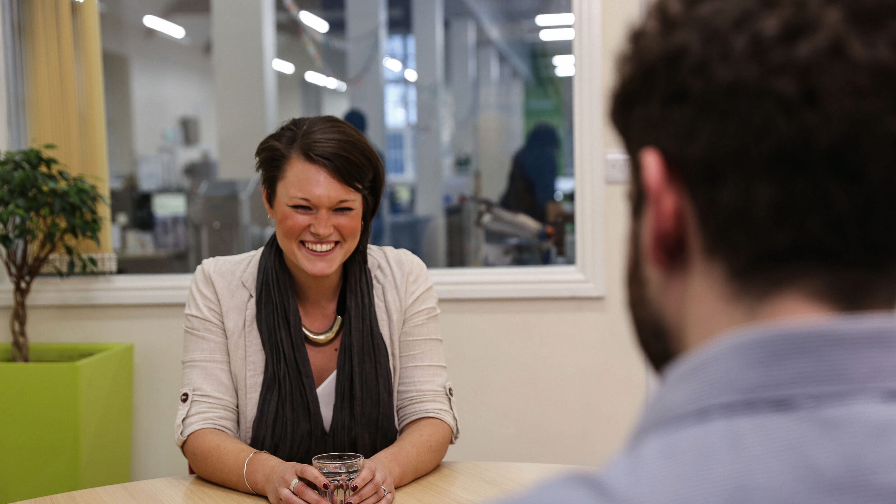 Young woman sat talking to male, laughing and smiling.