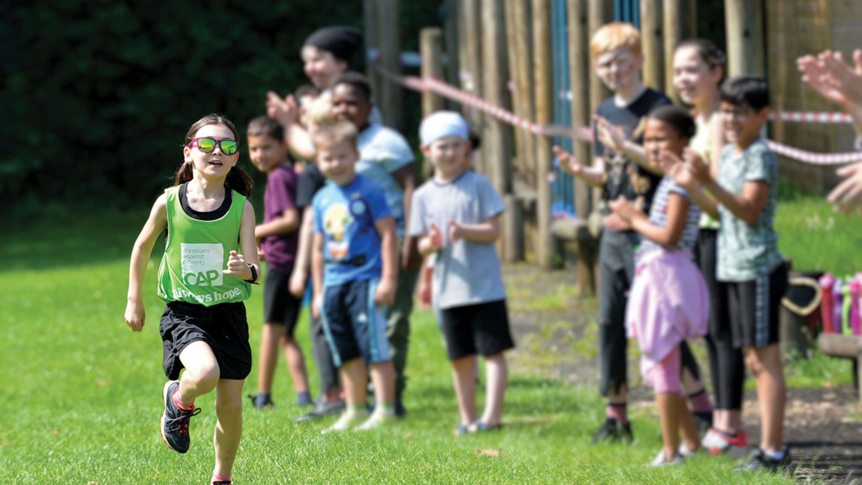 Young girl running in a bright green top as young girls and boys cheer her on.
