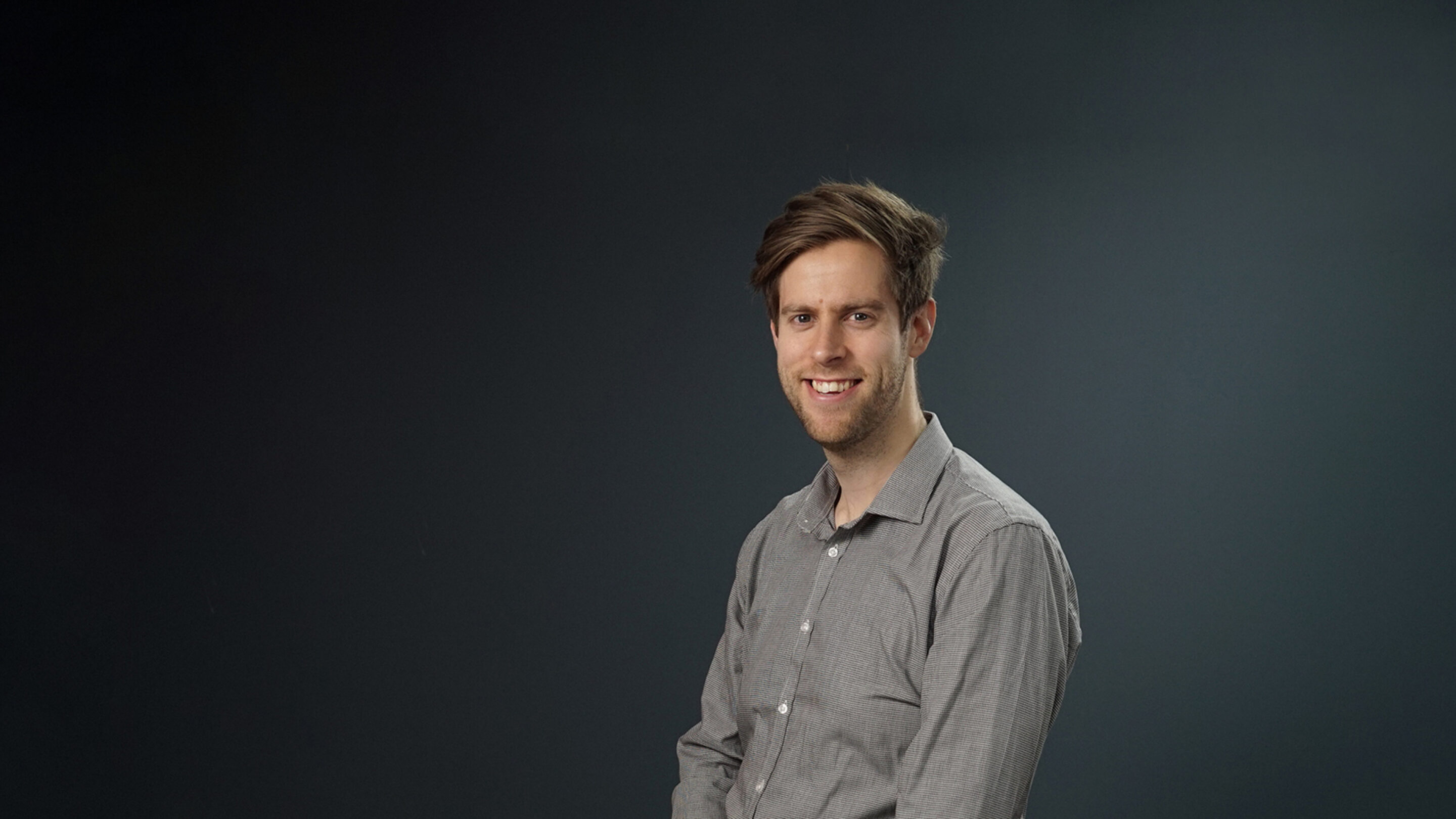 Young male sat side on looking towards the camera.