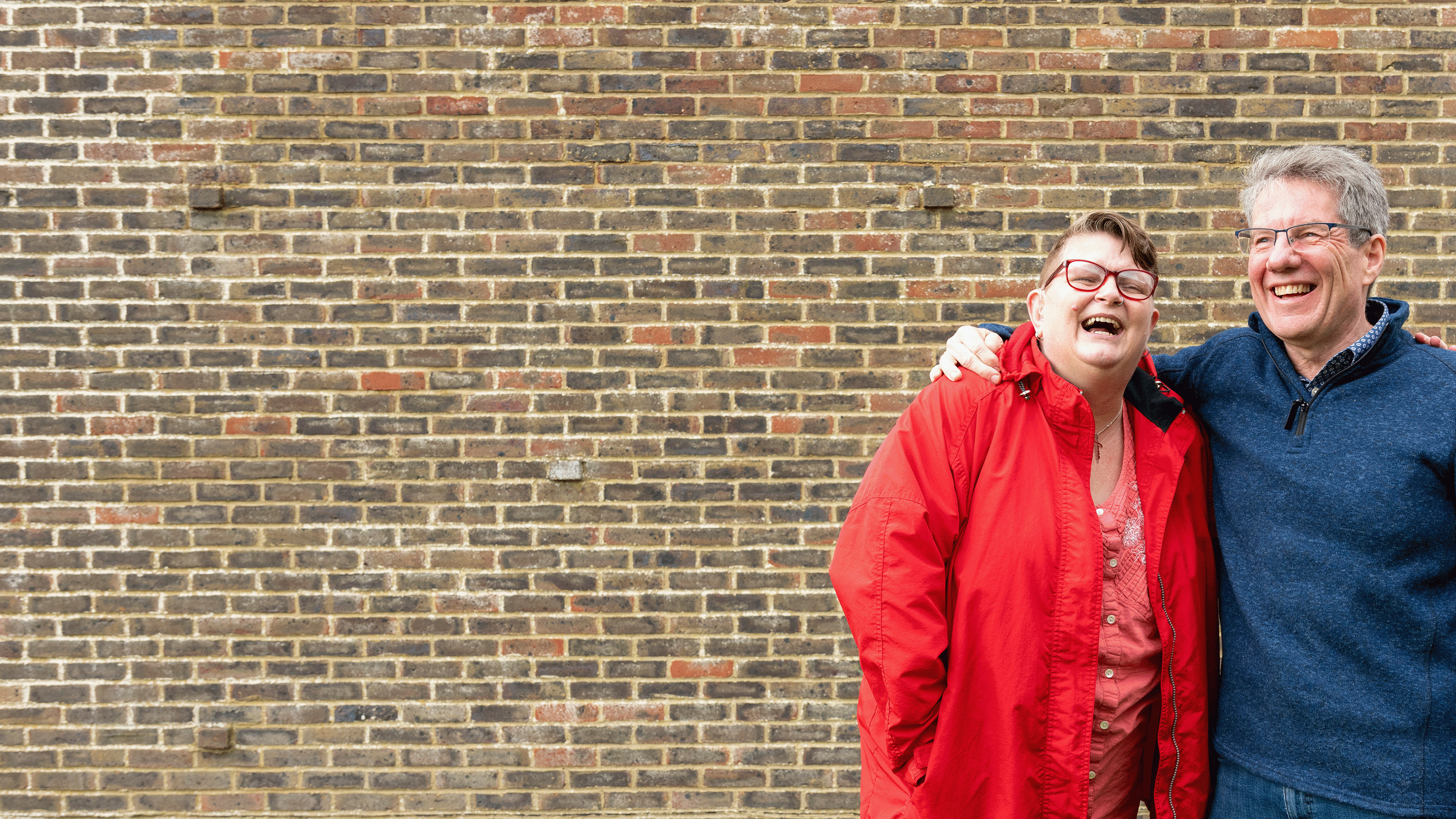 smiling couple in front of a red brick wall