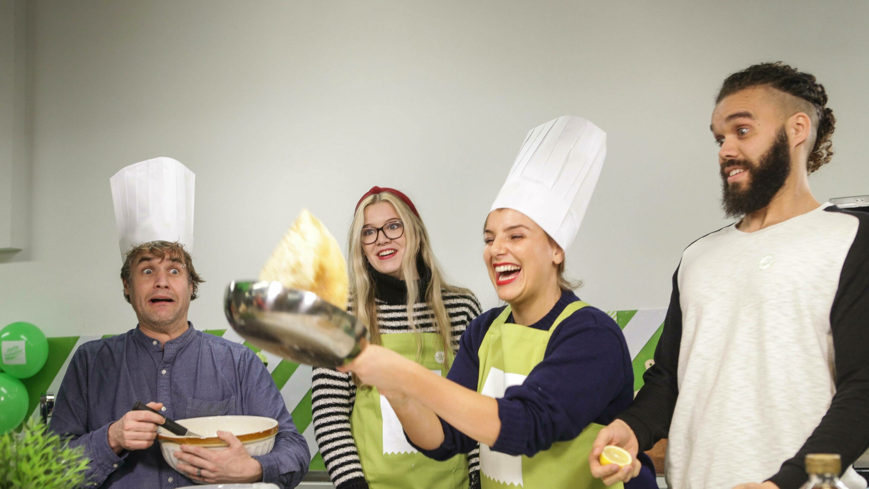 One female flipping a pancake while a group of male and females look shocked and excited.