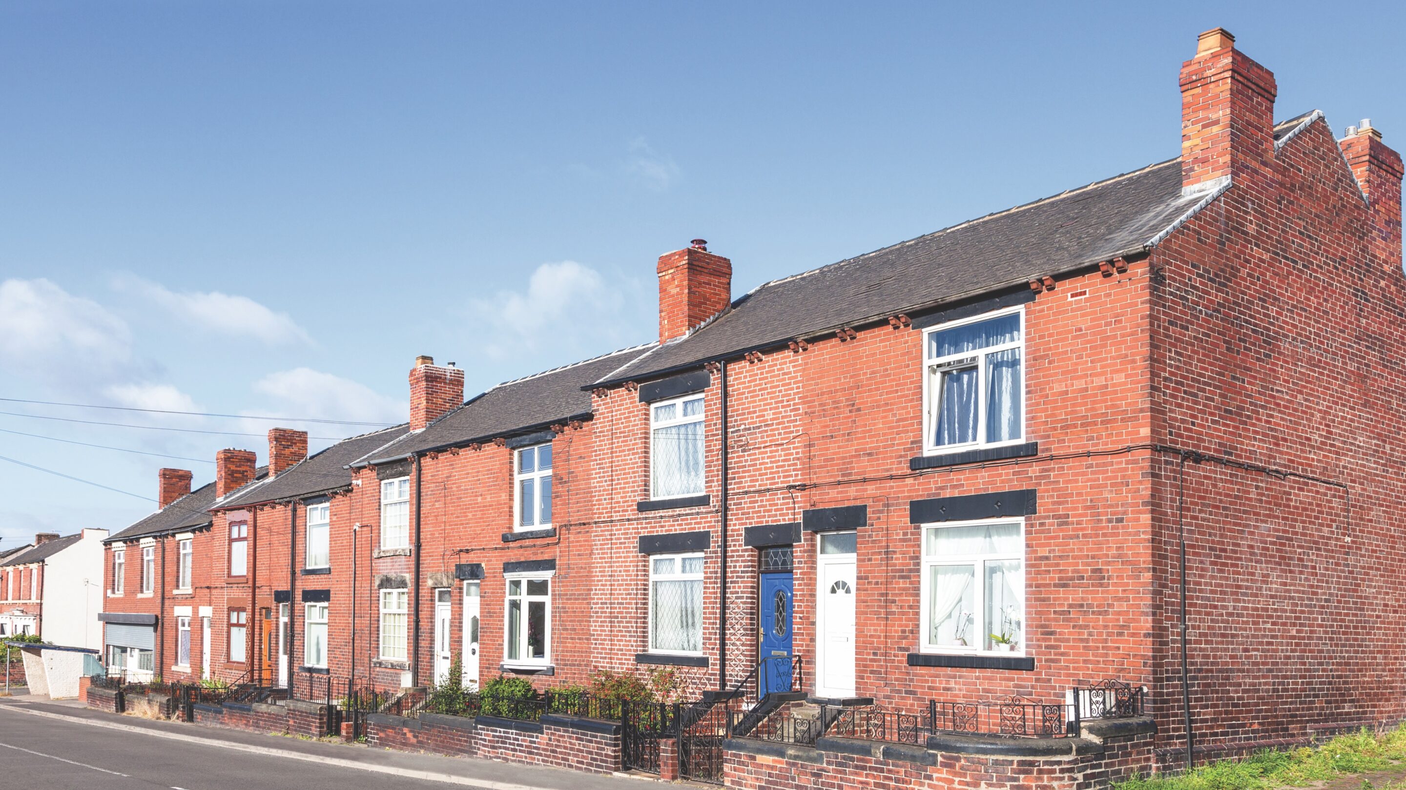 A row of brick terraced houses in the UK with a blue summer sky behind them.