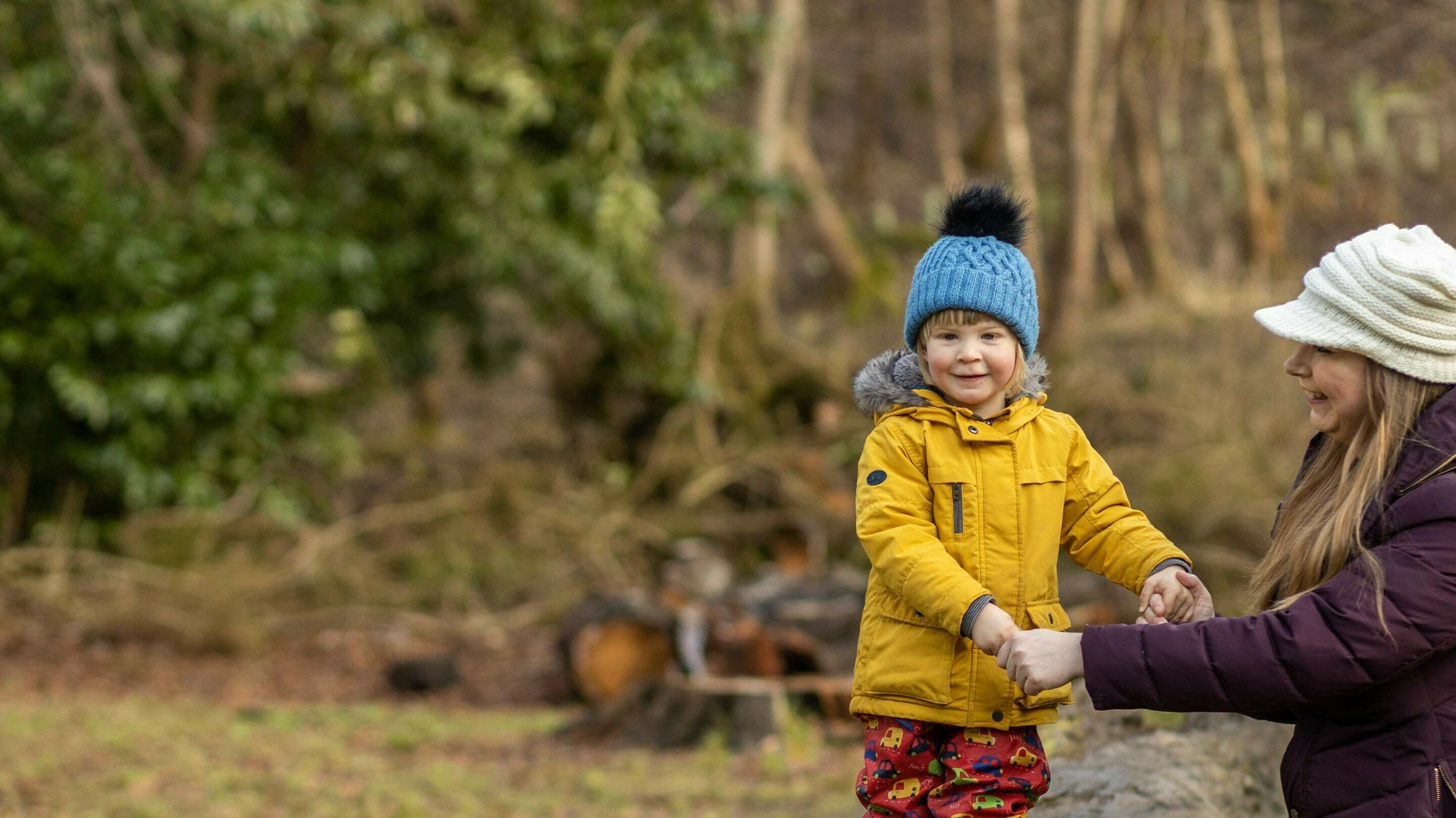 A mum helping her toddler son walk across a log in a forest, mum is smiling after becoming debt free with CAP.