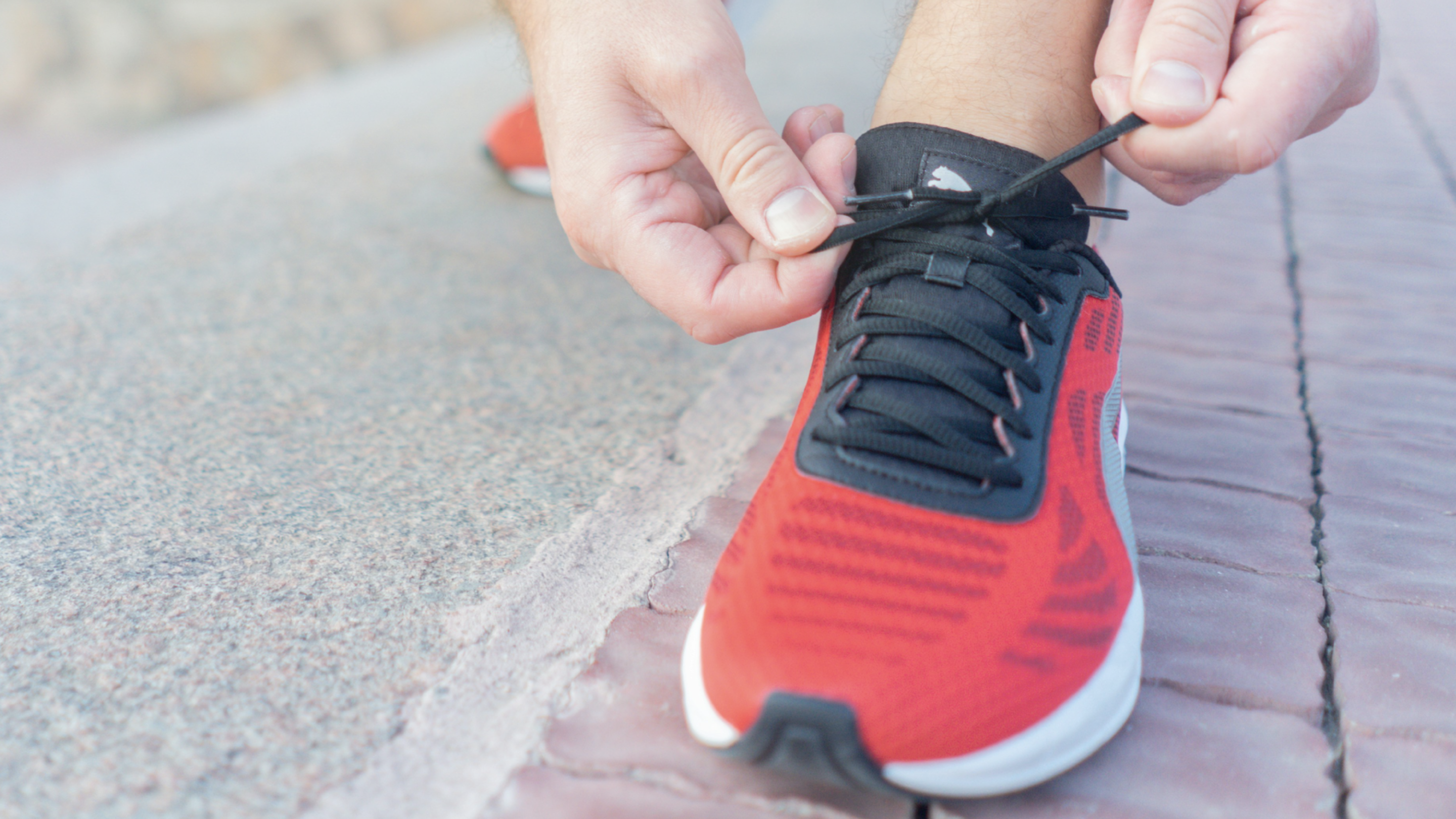 Person tying their shoelaces of their red and black running trainers