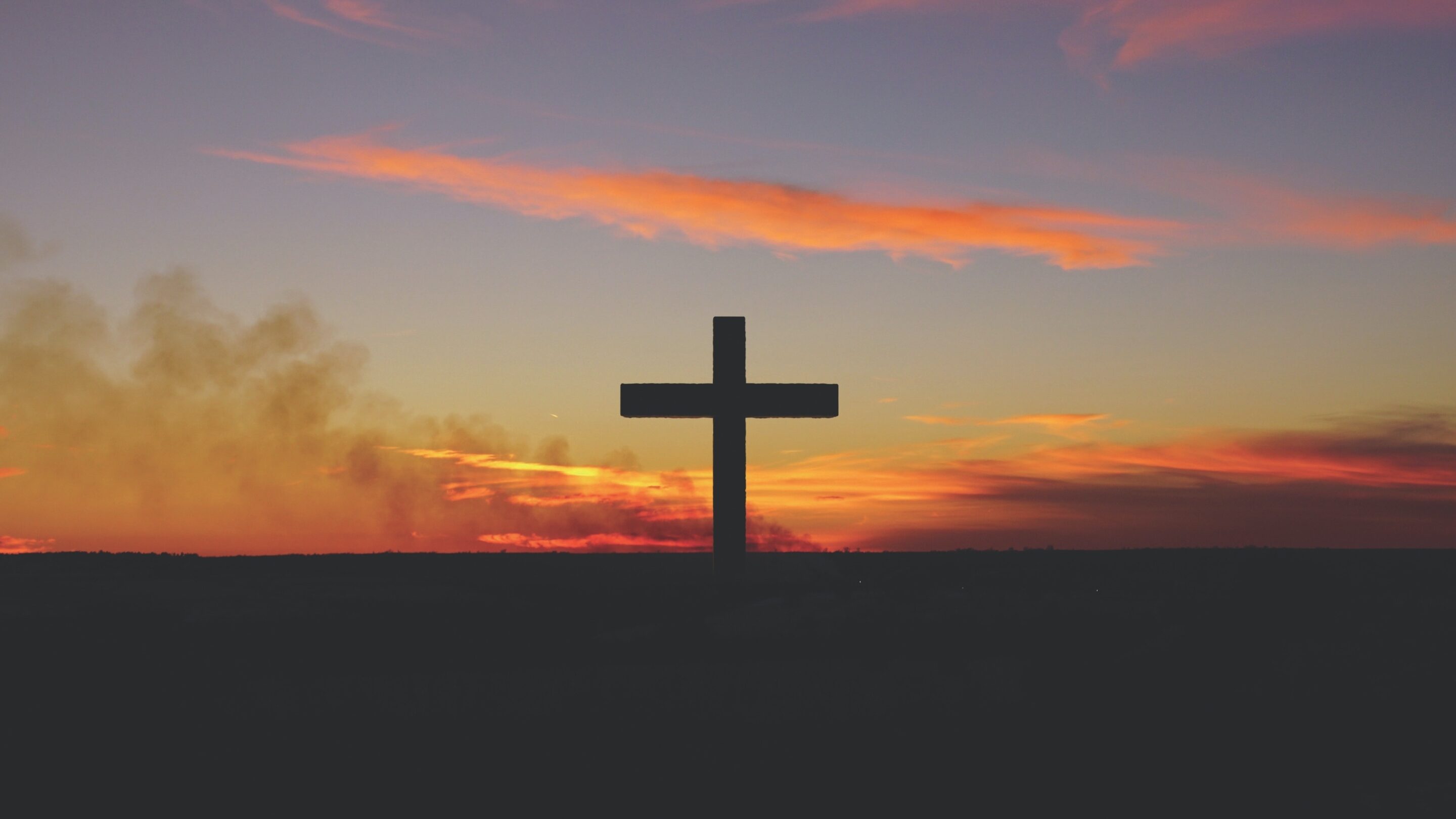 Cross with the sun setting behind, red and orange colours lighting up the clouds.