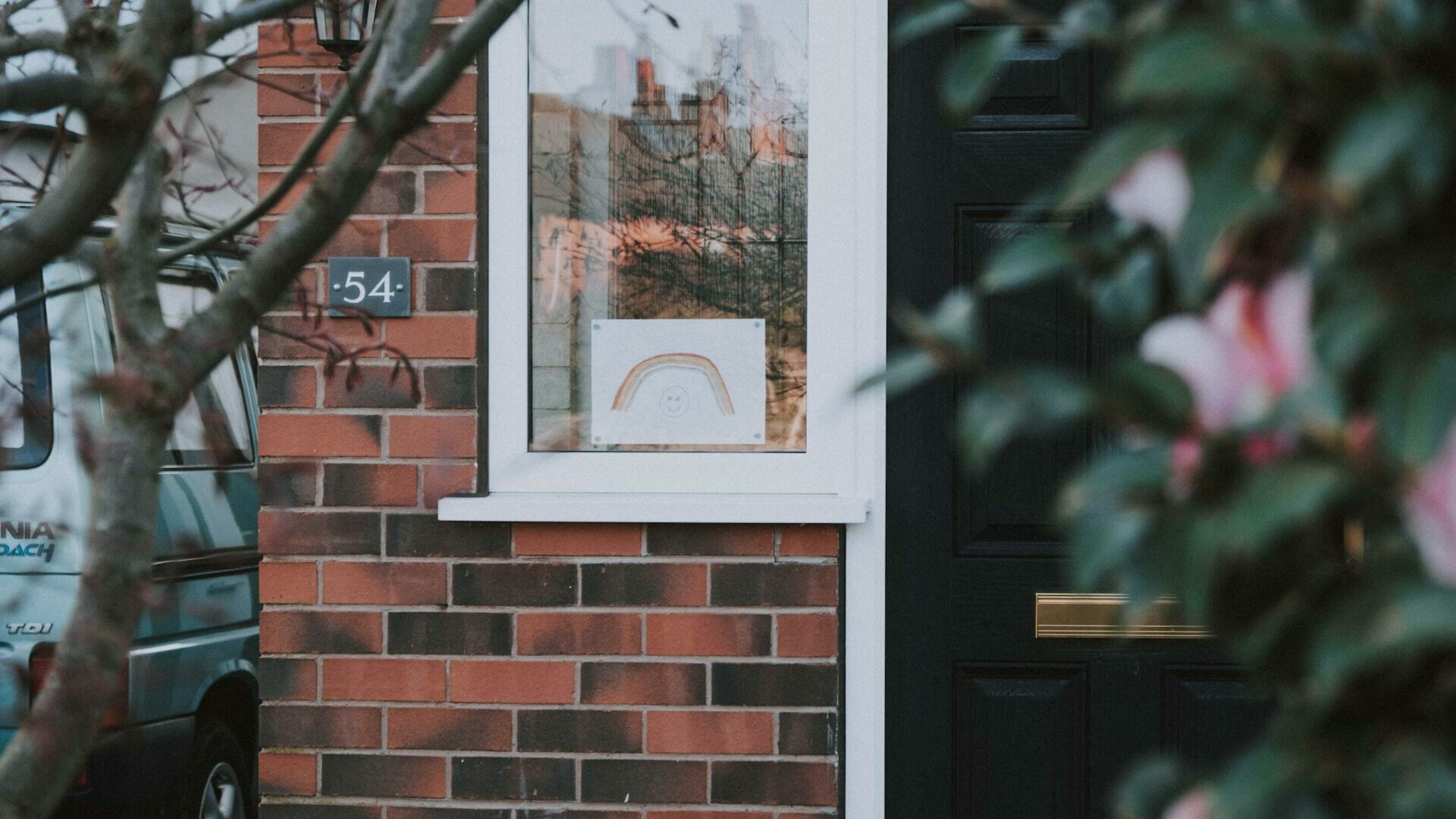 Front door of a house, a window is next to it with a child's hand drawn picture of a rainbow.