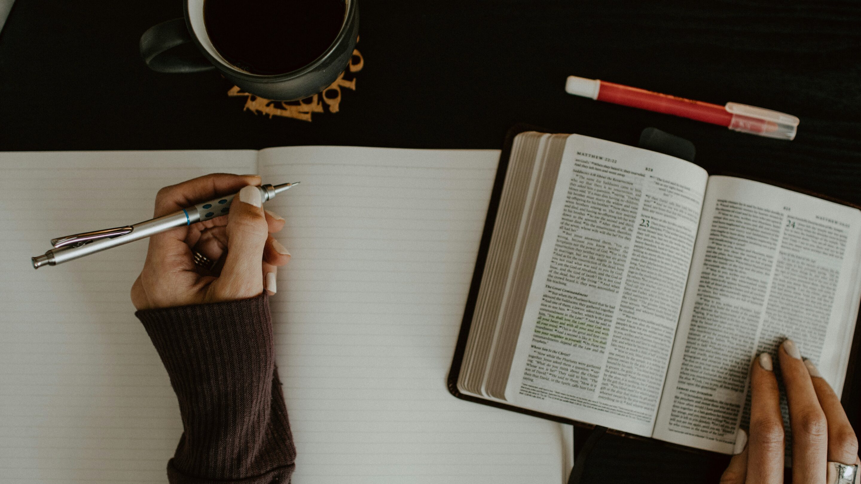 Person sat a desk with a prayer journal, Bible and coffee