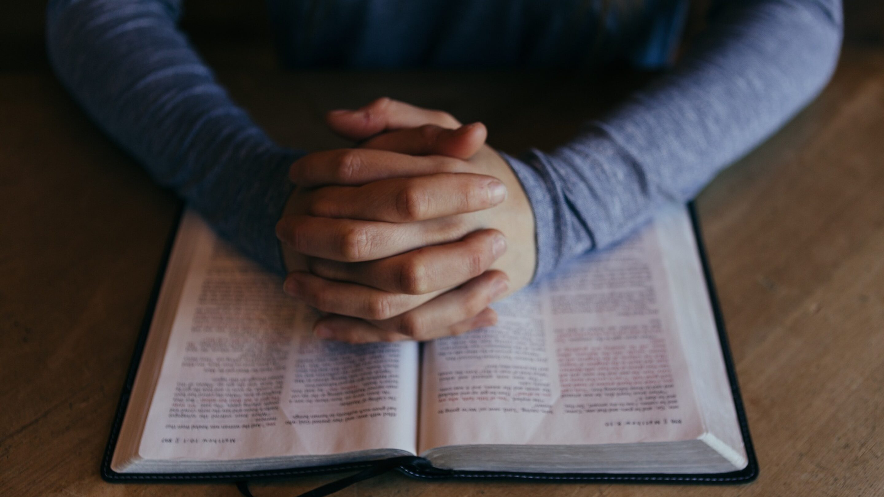 Woman with her hands clasped together in prayer, reading a Bible.