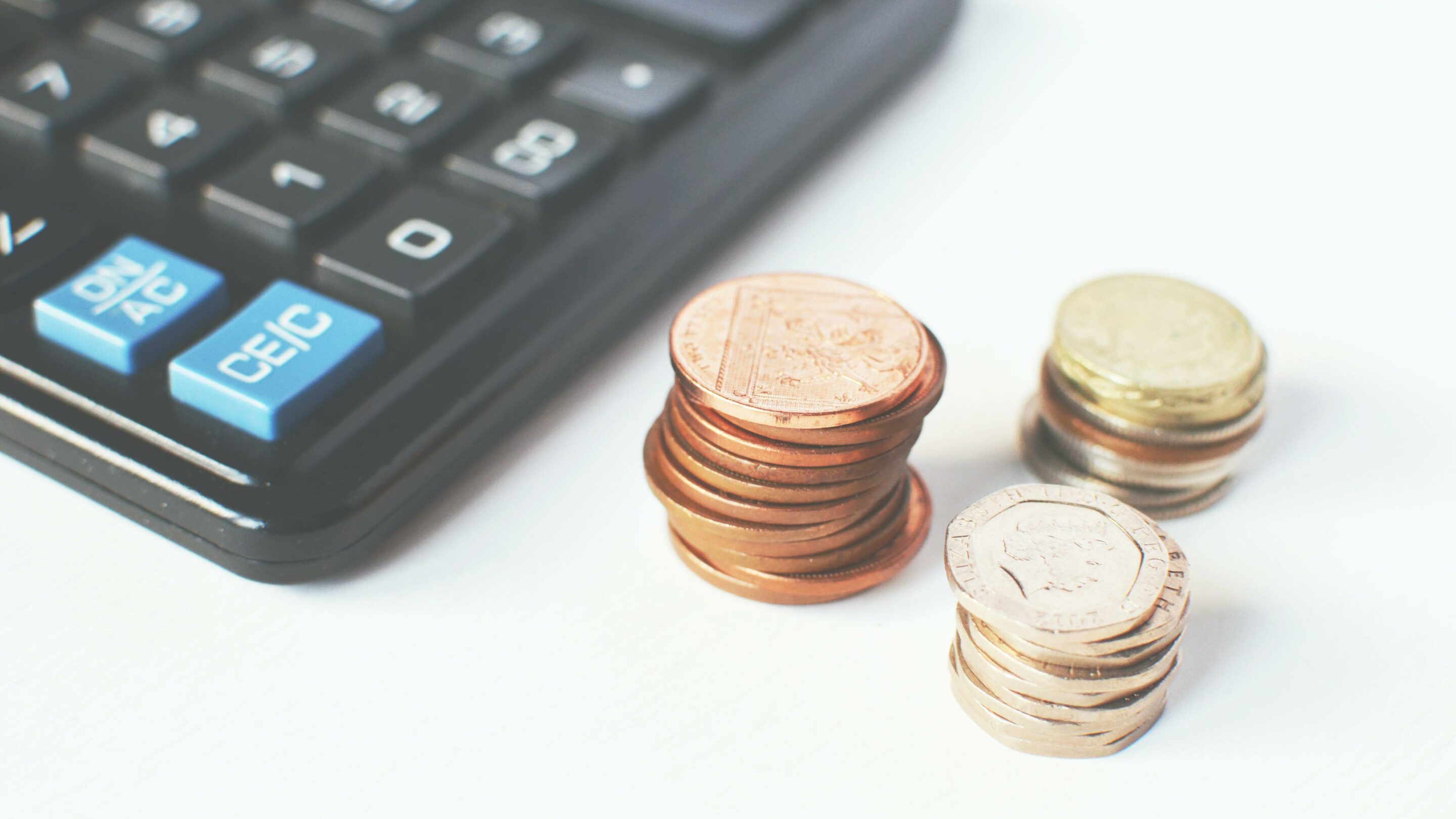 Three stacks of coins, two pennies, twenty pennies and pound coins, with a calculator next to them ready to create a budget.
