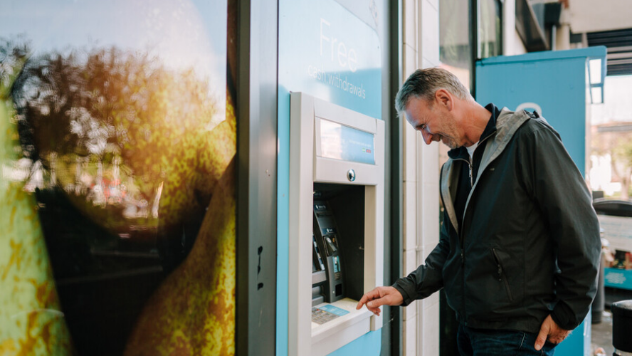A middle-aged man stood at a cash ATM, pressing the buttons and smiling