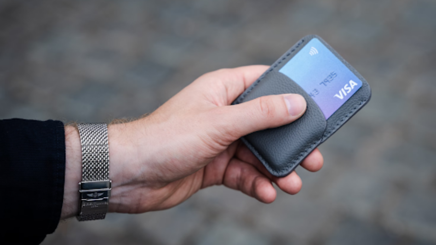 Image of a person's left hand, holding a wallet with a credit card in it