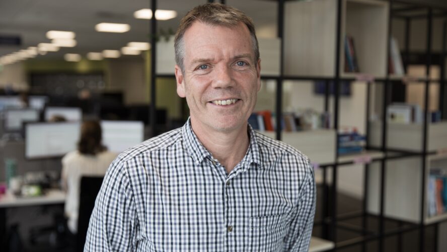 CAP Senior Debt Advisor, Jim, stood in CAP head office, smiling at the camera and wearing a check shirt.