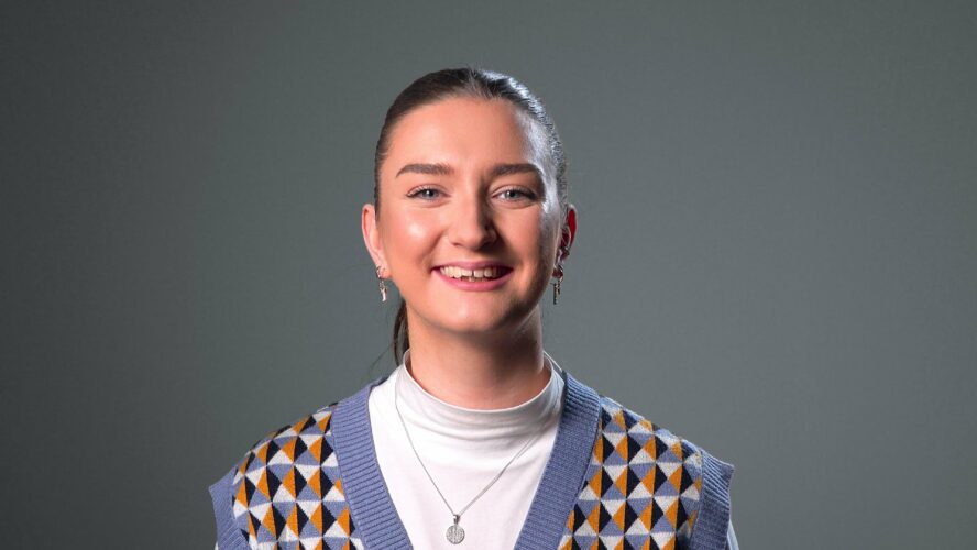 A younger CAP staff member smiling and stood in front of a grey background