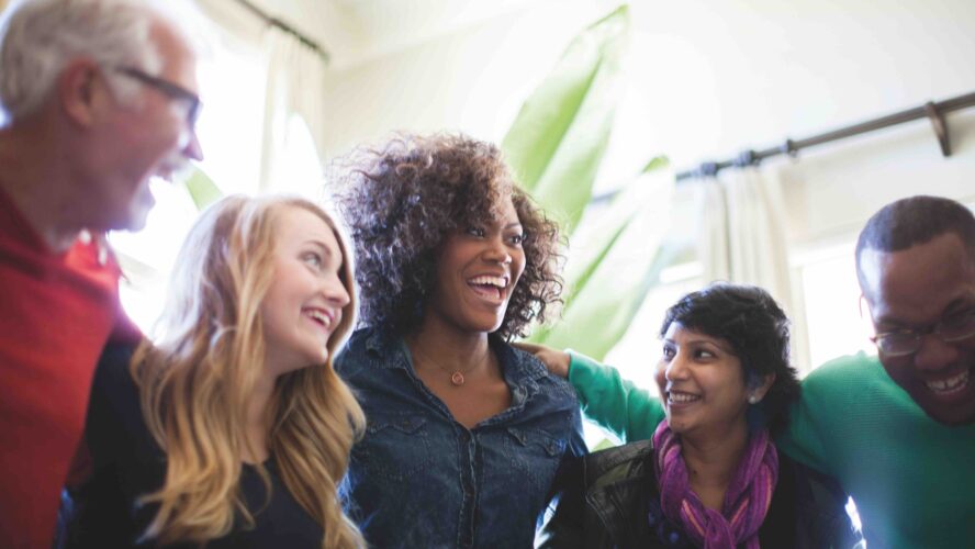 A group of both young and older males and females huddled in a group and laughing together.