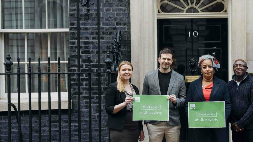 Two men and two women stood outside number 10 downing Street holding posters which say, hashtag look again, at UK poverty.