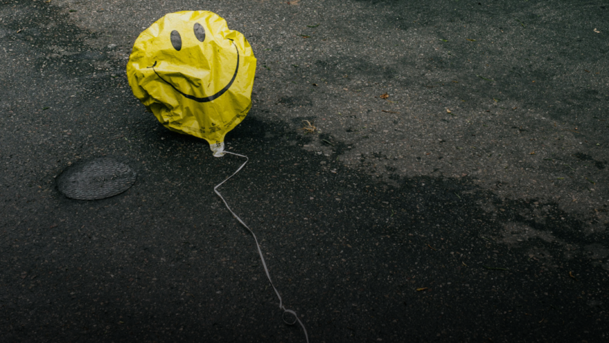 Yellow smiley face ballon lying on pavement deflated