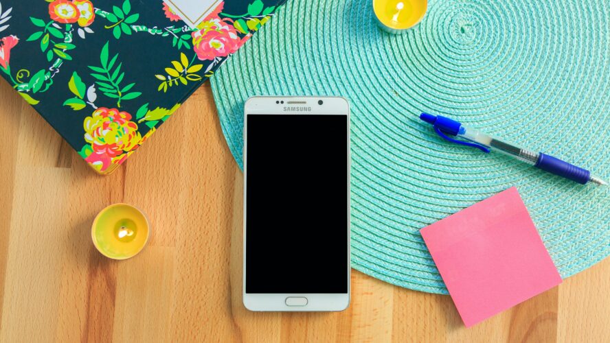 A phone on a desk next to a notebook, pen, and tealights