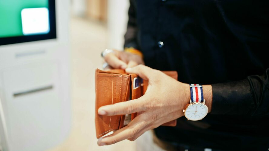 Male holding a wallet, reaching in to take money out of it.
