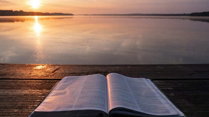 Picture of a Bible on a bench next to a lake, with the sun setting in the background