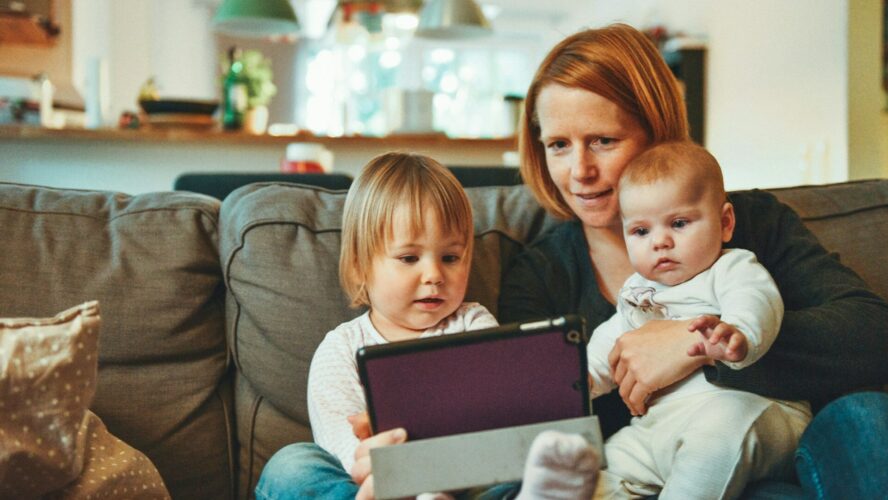 Mum and two young children sat on a sofa, all three of them are looking at a tablet.