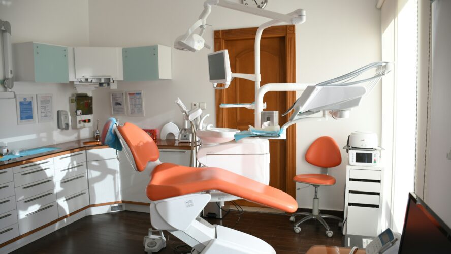 An empty dental treatment room with an orange dental chair in the middle