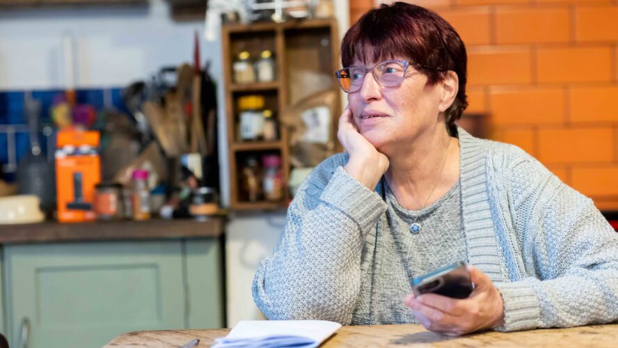 Older woman sat at a table looking at her phone and researching the Winter Fuel Payment.