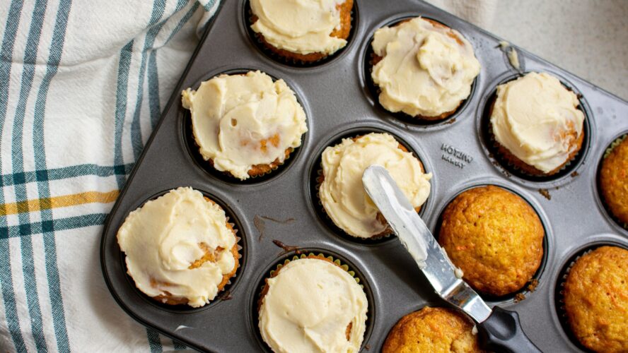 Plain cupcakes in a baking tin, with half of them covered with buttercream