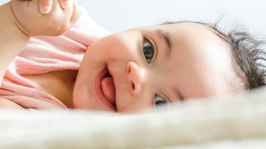 A baby girl ages around 6 months, laying on her side and smiling