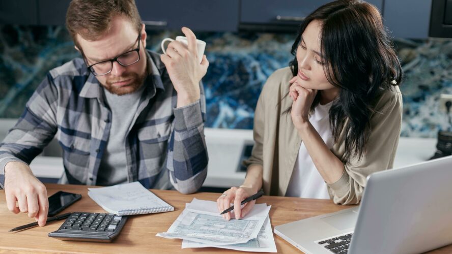 A man and a woman sat next to each other at a table, looking at a calculator and their finance documents.