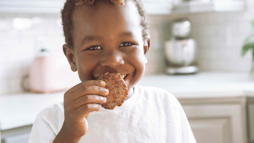 A little boy smiling and holding up a cookie he got in a kids eat for free deal.
