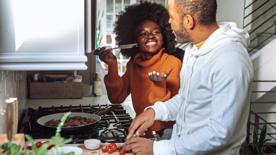 A couple in the kitchen cooking together and smiling at each other.