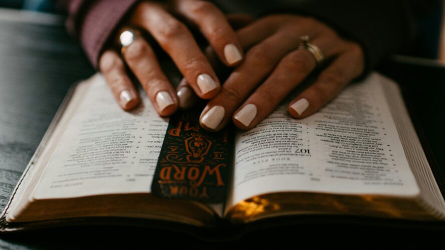An open bible with gold sprayed edges, and a person's hands resting on top of it