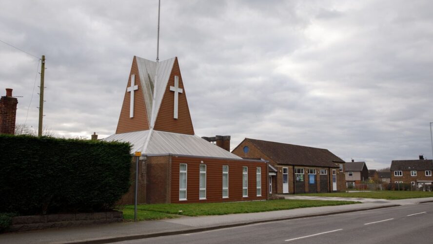 Photo of the outside of a UK parish church, with a white cross on the top