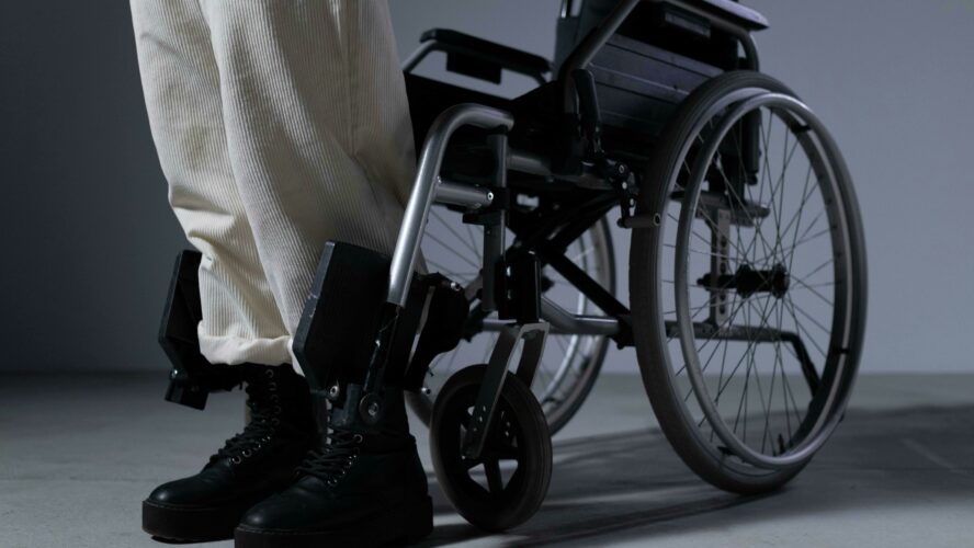 Image showing a wheelchair against a grey background and a person getting out of it