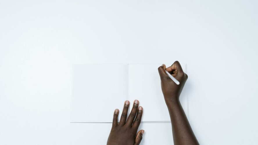 Two hands holding a pen writing on a blank piece of paper.