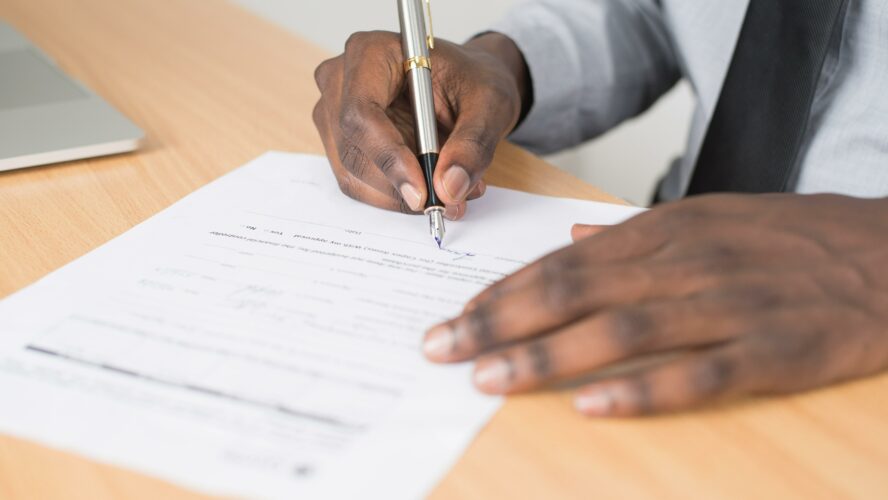 Hands signing a document with a pen.